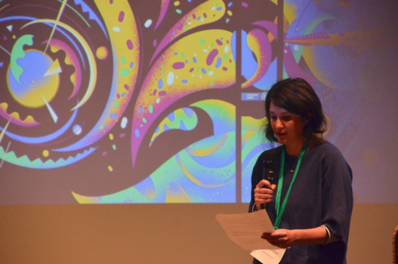 Silvia Garbari spricht am Mikrofon vor einem bunten Hintergrund
